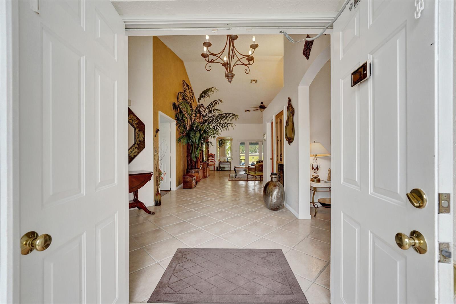 A view through an open doorway into a tiled foyer with a chandelier and plant — 3460 Dunes Vista Drive, Pompano Beach FL 33069, POMPANO BEACH, FL