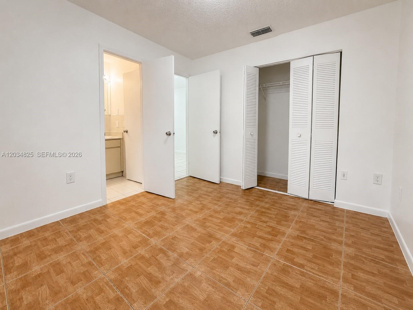An empty bedroom features white walls, wood-look tile flooring, a closet, and two doorways — 2485 W 70th Pl, Hialeah FL 33016, HIALEAH, FL