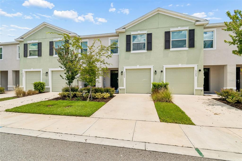 The exterior of a townhouse features a light green garage, a black front door, and landscaping — 17245 AMBER ASPEN WAY, LAND O LAKES, FL