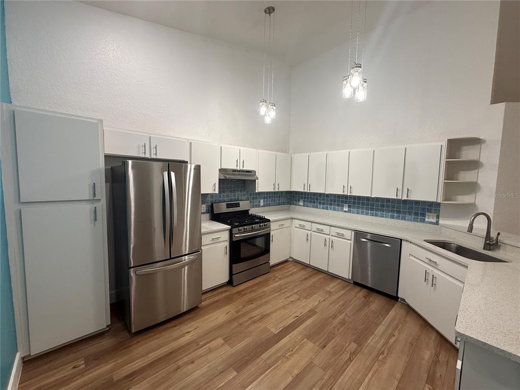 A kitchen features white cabinets, stainless steel appliances, a blue tiled backsplash, and wood flooring — 21542 CLUBSIDE LOOP, LUTZ, FL
