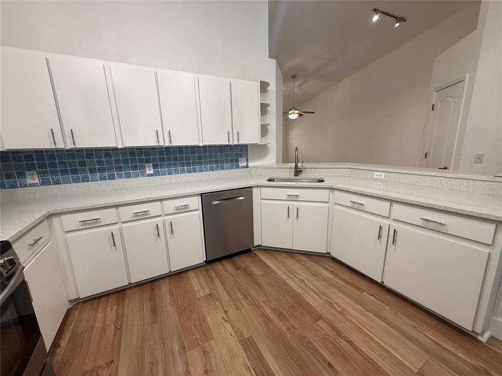 A kitchen features white cabinets, light countertops, a blue tiled backsplash, and wood-look flooring — 21542 CLUBSIDE LOOP, LUTZ, FL