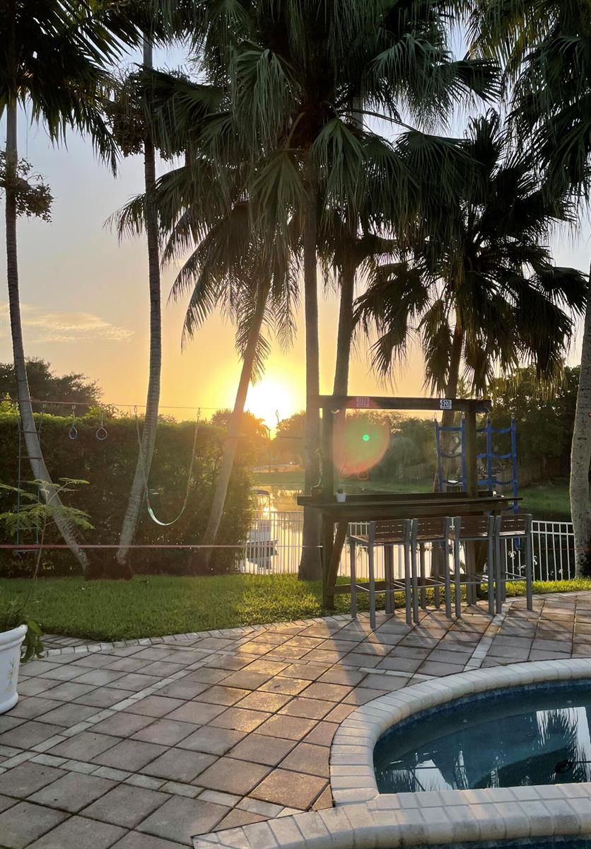 A backyard patio features a wooden bar, palm trees, and a view of a sunset — 11380 Wayne Drive, Cooper City FL 33026, COOPER CITY, FL