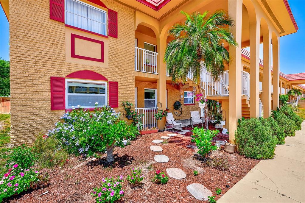 The exterior of a multi-story apartment building features a landscaped garden with stone pathways — 1300 S HERCULES AVENUE UNIT 1, CLEARWATER, FL