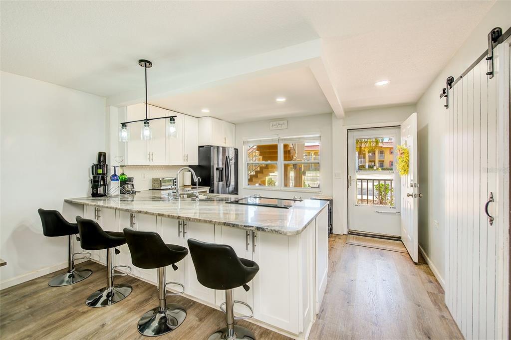 A kitchen with white cabinets, a marble-topped island with bar stools, and an exterior door — 1300 S HERCULES AVENUE UNIT 1, CLEARWATER, FL