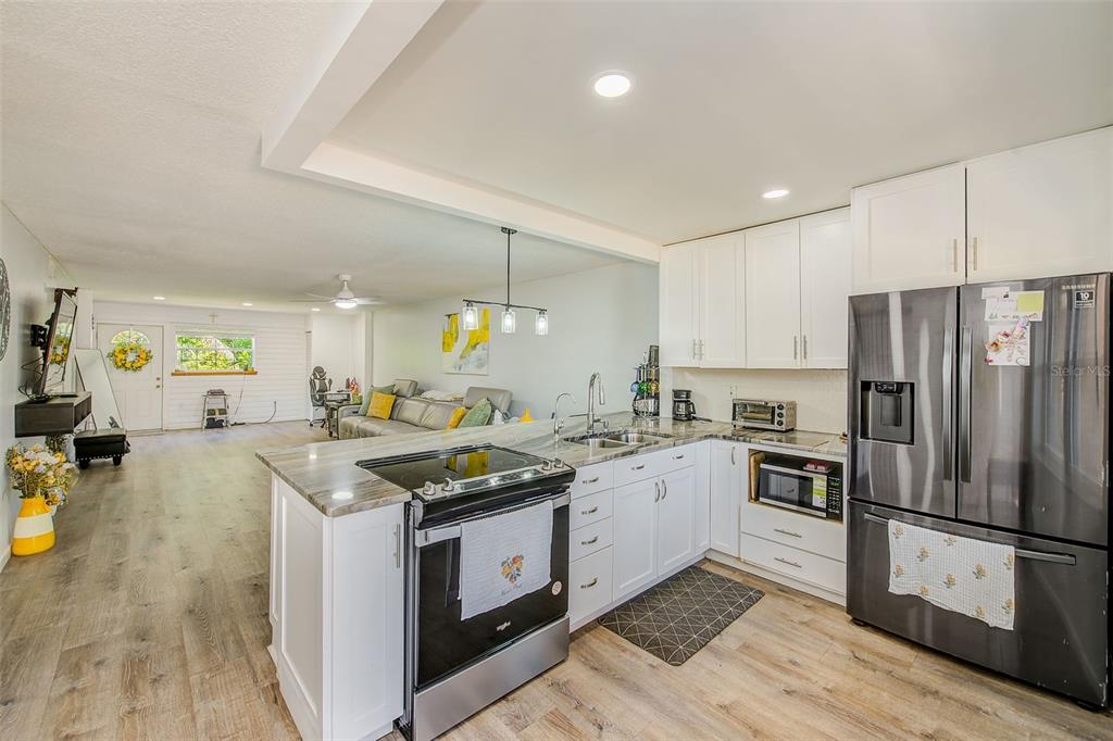 A kitchen with white cabinets, stainless steel appliances, and a peninsula overlooks an open living area — 1300 S HERCULES AVENUE UNIT 1, CLEARWATER, FL