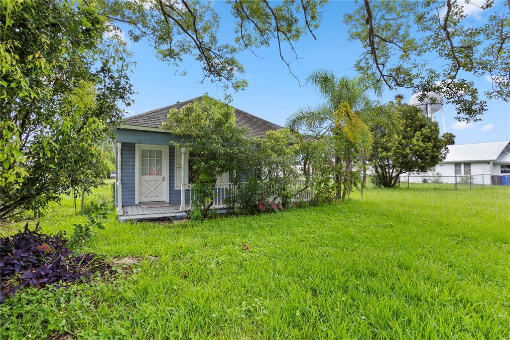 A blue house with a front porch sits on a grassy lot under large trees — 1418 MASSACHUSSETTS AVENUE, ST CLOUD, FL