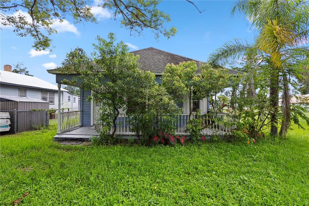 A blue house with a front porch and white railing sits behind overgrown landscaping — 1418 MASSACHUSSETTS AVENUE, ST CLOUD, FL