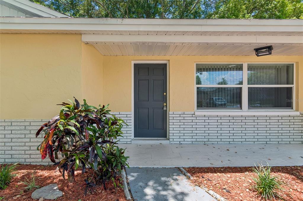 The exterior of a house features a yellow facade, a gray door, and white brick — 7105 OAKSHIRE DRIVE, PORT RICHEY, FL