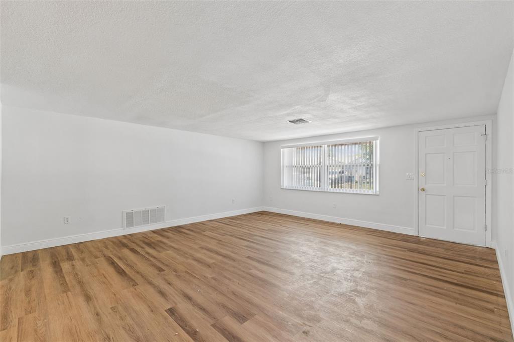 An empty room with white walls, wood-look flooring, a window with blinds, and a door — 7105 OAKSHIRE DRIVE, PORT RICHEY, FL