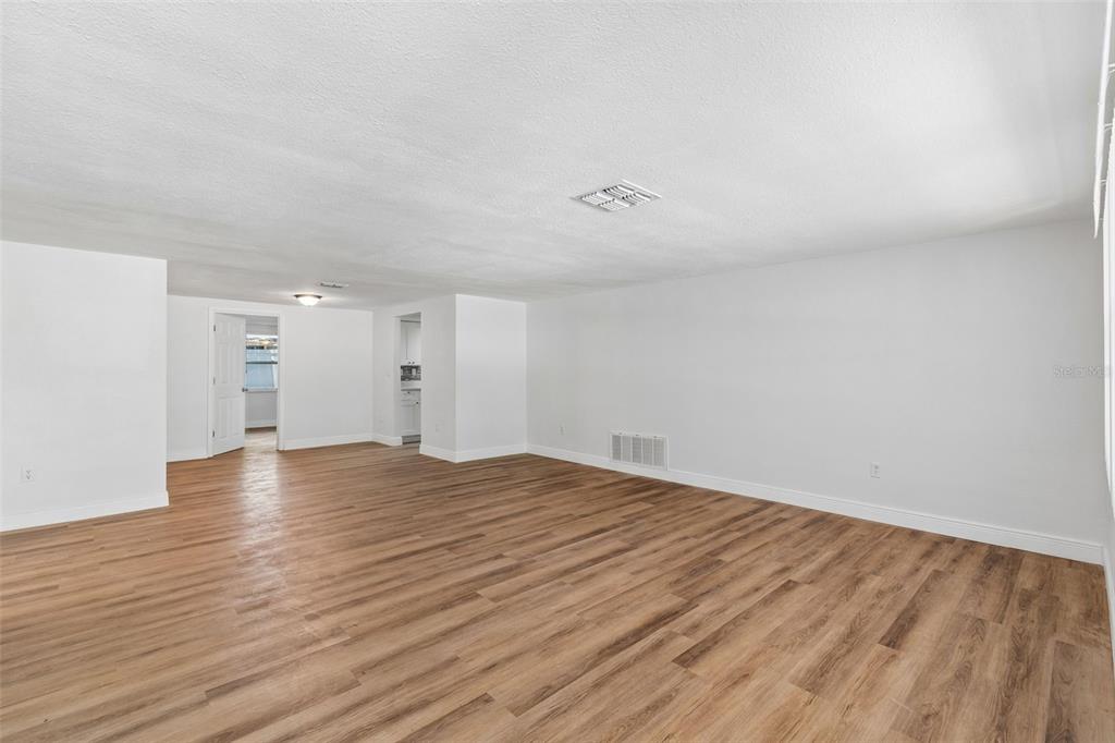 A spacious, empty room features light wood-look flooring, white walls, and a recessed ceiling vent — 7105 OAKSHIRE DRIVE, PORT RICHEY, FL
