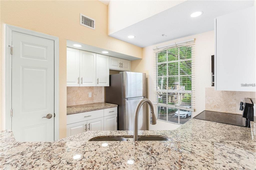 A kitchen features white cabinetry, granite countertops, a stainless steel refrigerator, and a window view — 6308 RALEIGH STREET UNIT 311, ORLANDO, FL