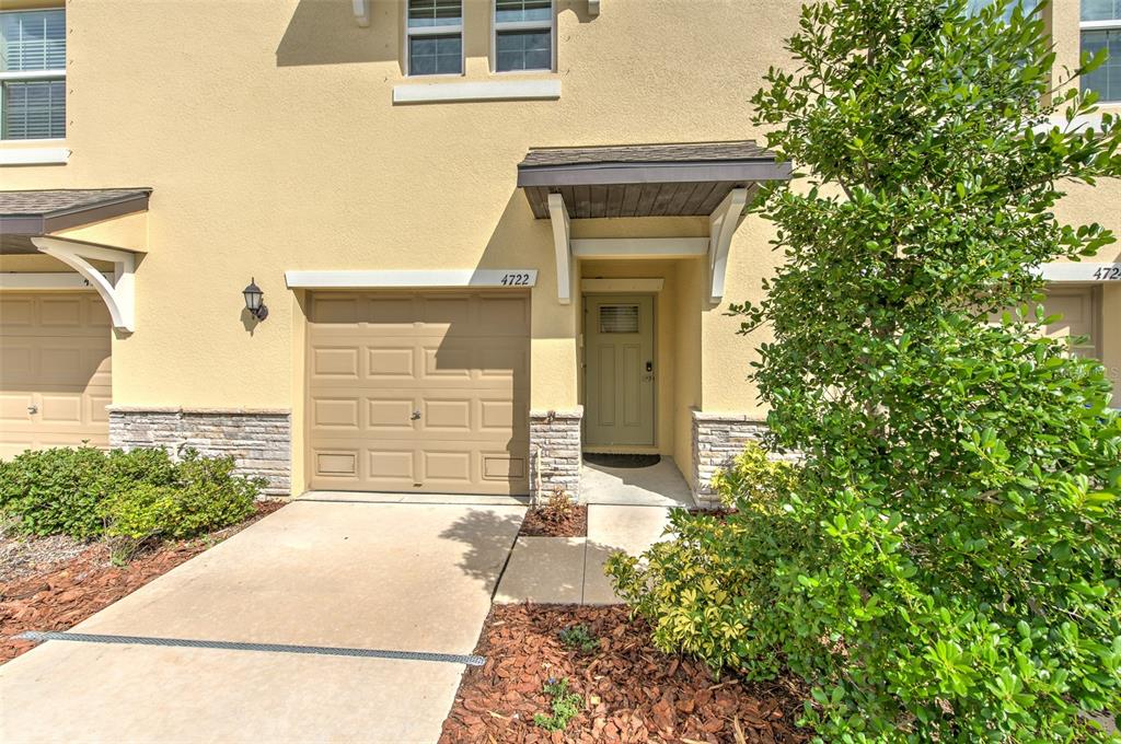 A tan townhome exterior features a single-car garage, a front door, and a small tree — 4722 TUSCAN LOON DRIVE, TAMPA, FL