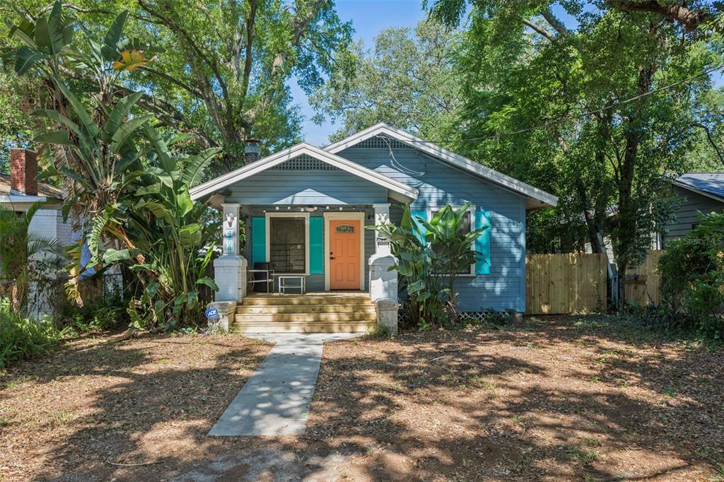A blue bungalow with a front porch, orange door, and turquoise shutters sits among trees — 4208 N MARGUERITE, TAMPA, FL