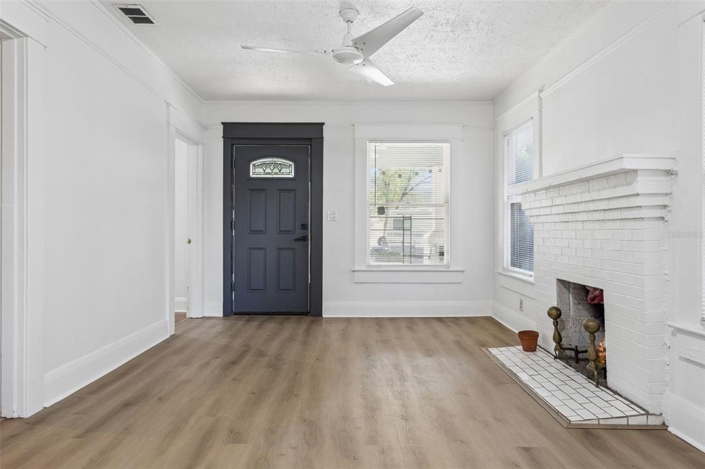 A living room features white walls, wood-look flooring, a white brick fireplace, and a dark door — 4208 N MARGUERITE, TAMPA, FL
