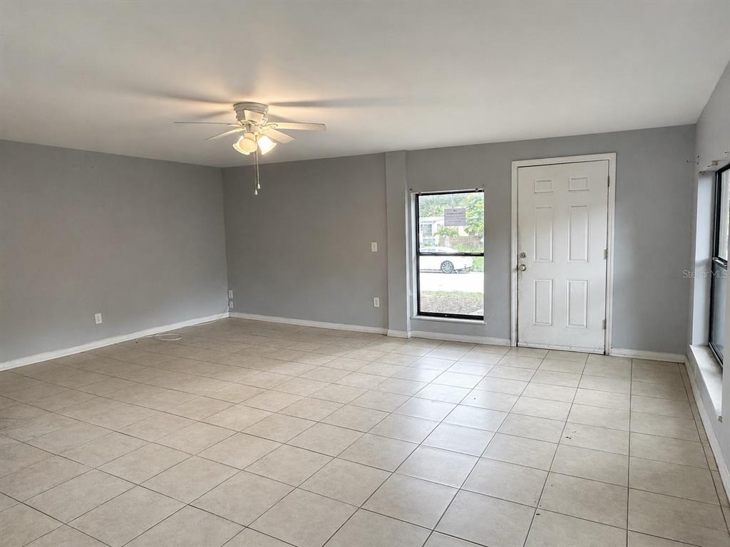 An empty living room features gray walls, light-colored tile flooring, a ceiling fan, and a door — 1519 LYNN AVENUE, CLEARWATER, FL
