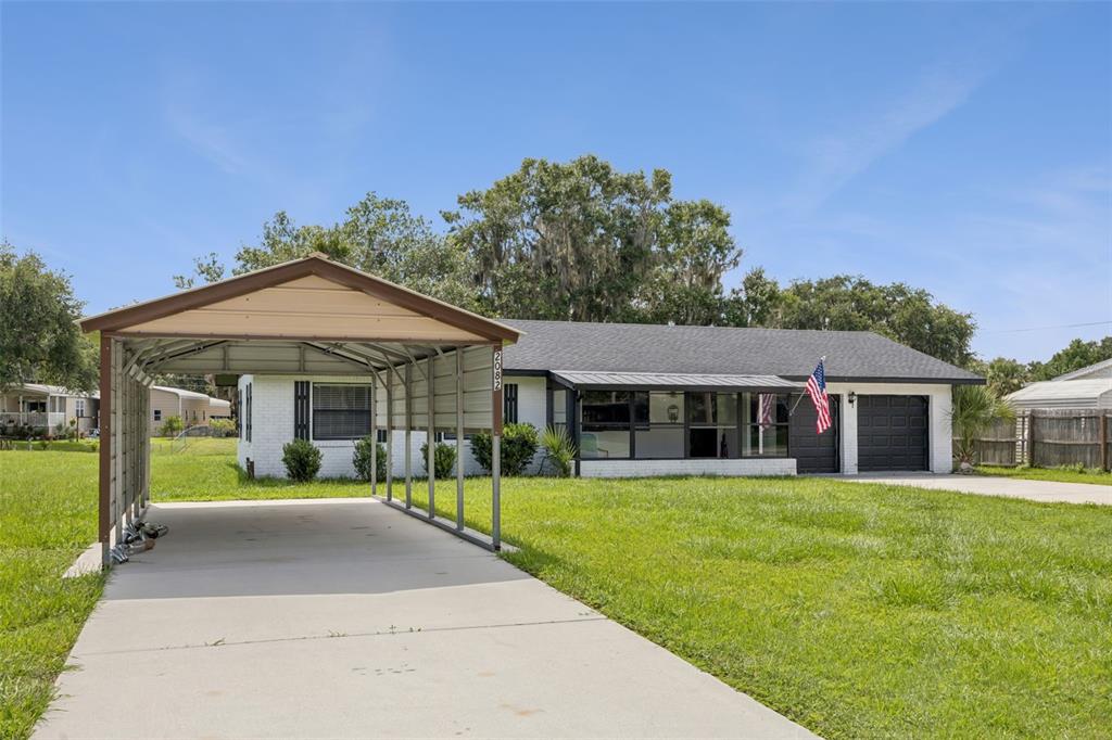 A single-story white brick house features a metal carport and a front porch — 2082 SHADY LANE, GENEVA, FL