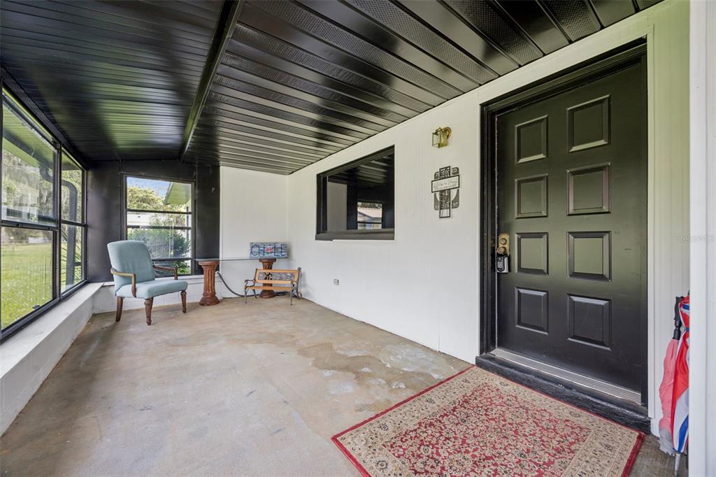 A covered porch features a black front door, concrete flooring, and a light blue chair — 2082 SHADY LANE, GENEVA, FL