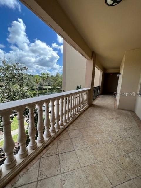 A covered balcony features a stone-tiled floor, a decorative balustrade, and a view of trees — 7710 LAKE VISTA COURT UNIT 303, LAKEWOOD RANCH, FL