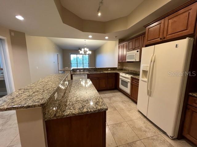 A kitchen features granite countertops, wood cabinetry, tile flooring, and a white refrigerator — 7710 LAKE VISTA COURT UNIT 303, LAKEWOOD RANCH, FL