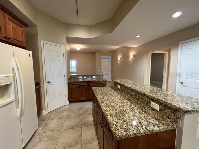 A kitchen features granite countertops, wood cabinetry, and tile flooring — 7710 LAKE VISTA COURT UNIT 303, LAKEWOOD RANCH, FL