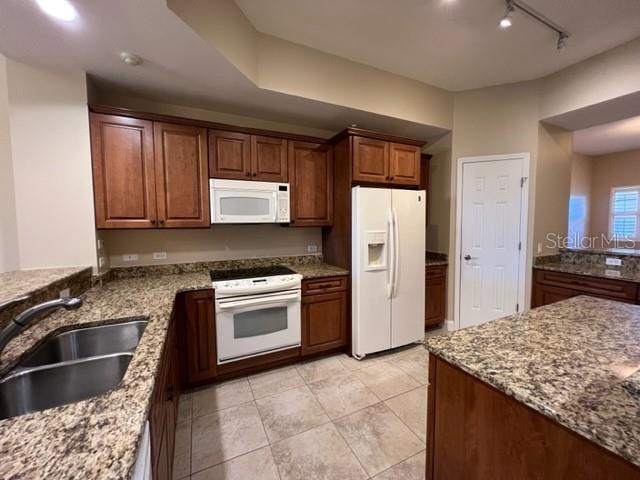 A kitchen features wood cabinets, granite countertops, stainless steel appliances, and tile flooring — 7710 LAKE VISTA COURT UNIT 303, LAKEWOOD RANCH, FL