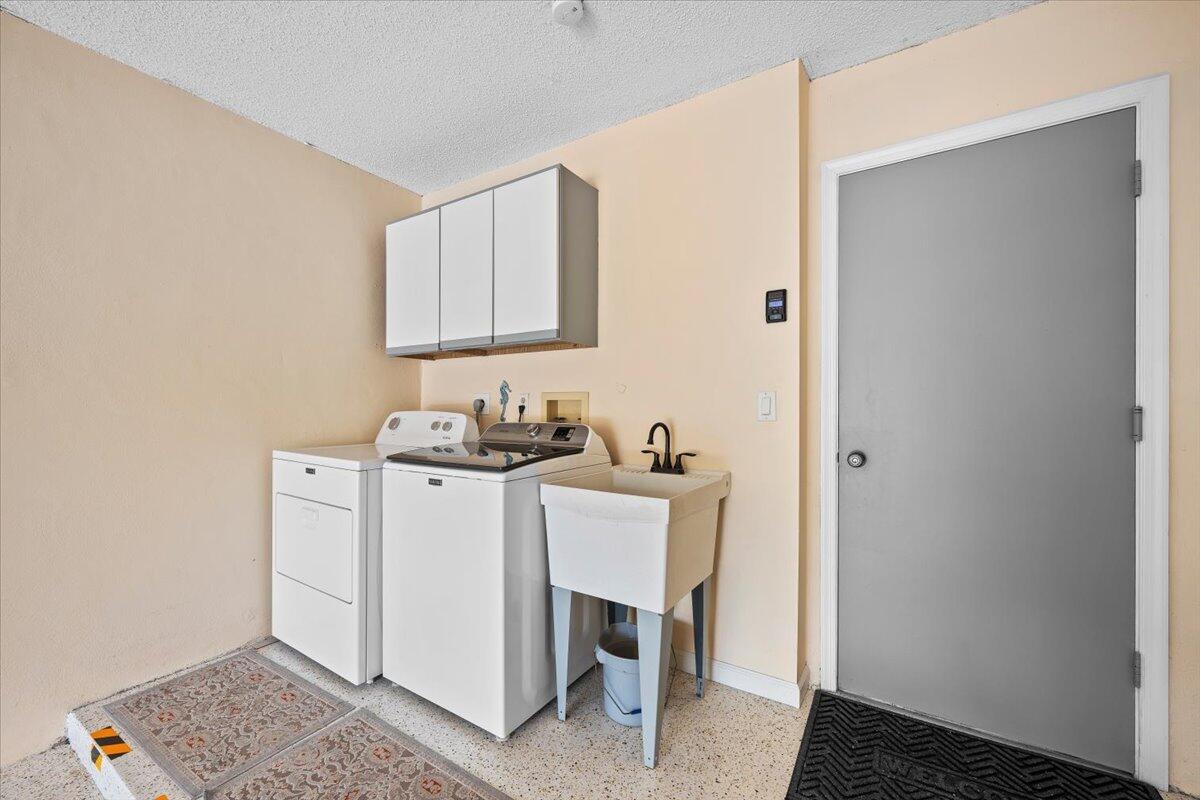 A laundry room features a washer, dryer, utility sink, white cabinets, and a gray door — 16913 Waterbend Drive # 165, Jupiter FL 33477, JUPITER, FL