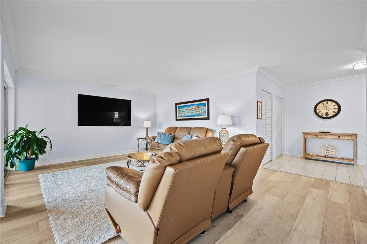 A living room features light wood flooring, a tan leather sofa, and a wall-mounted television — 16913 Waterbend Drive # 165, Jupiter FL 33477, JUPITER, FL