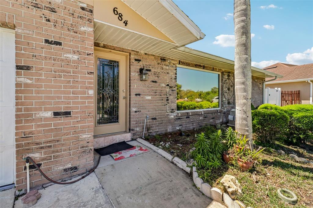 A brick house exterior features a front door with decorative glass and a large window — 684 REILLYS ROAD, PORT ORANGE, FL