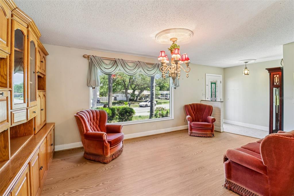 A living room features wood-look flooring, a large window, a chandelier, and three velvet chairs — 684 REILLYS ROAD, PORT ORANGE, FL