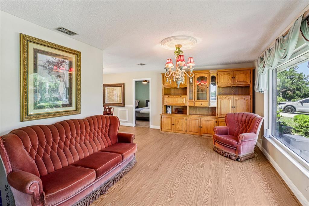 A living room features a velvet sofa, matching armchair, wood-toned cabinetry, and a chandelier — 684 REILLYS ROAD, PORT ORANGE, FL