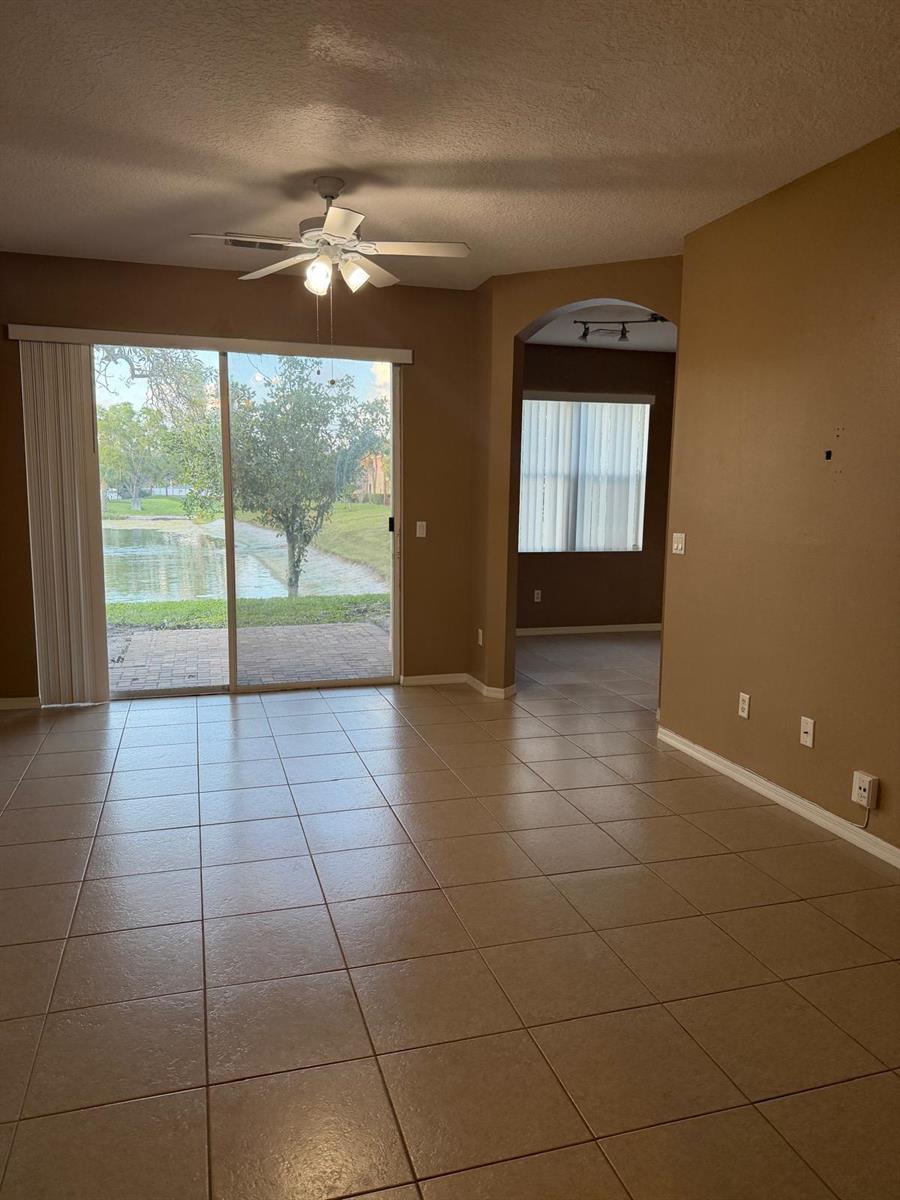 An empty living room with tan tile floors, a ceiling fan, and sliding glass patio doors — 1510 Seminole Palms Drive, FL 33463, FL