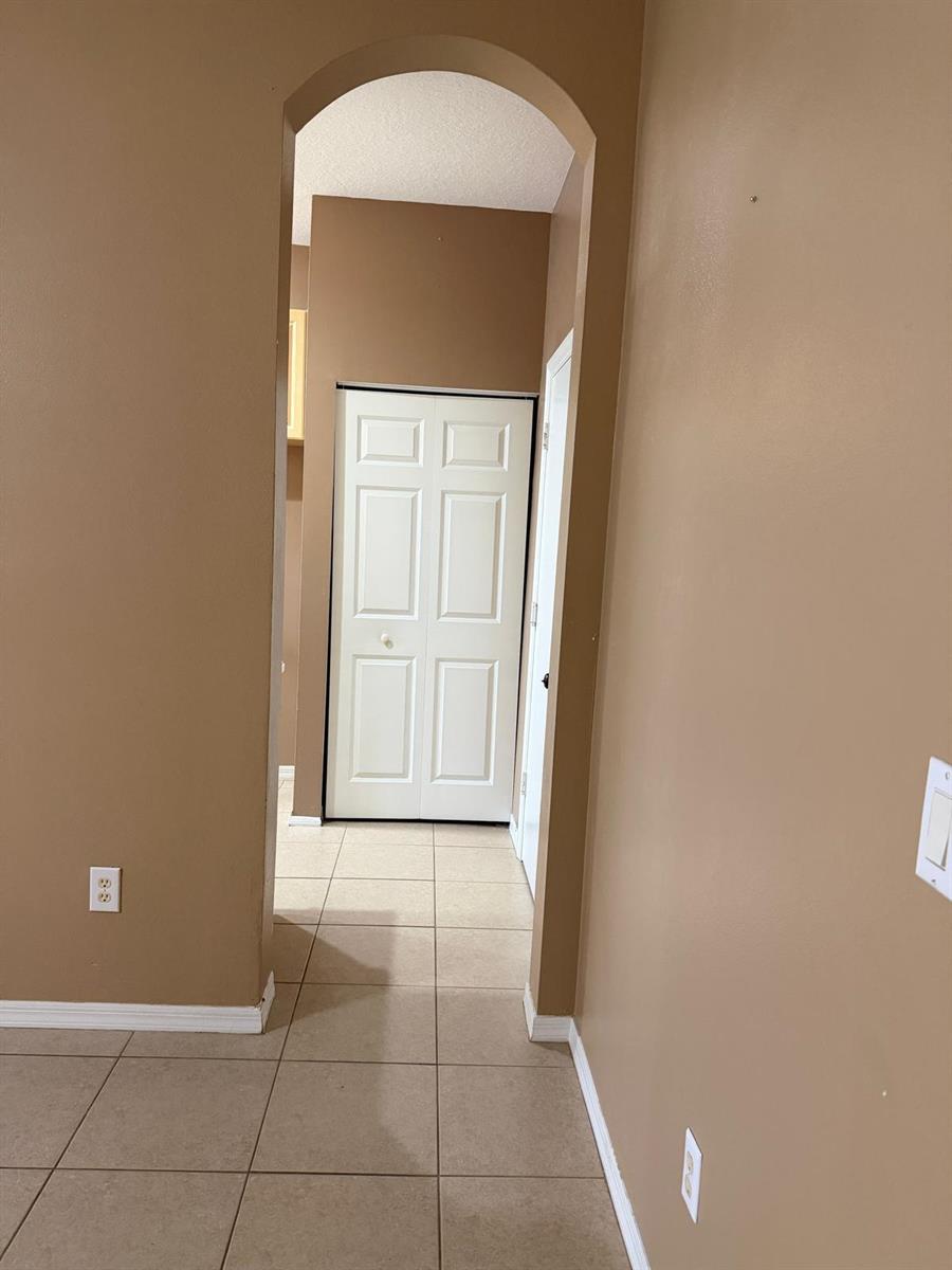 A hallway with tan walls, tile flooring, and an arched entryway leads to a white door — 1510 Seminole Palms Drive, FL 33463, FL