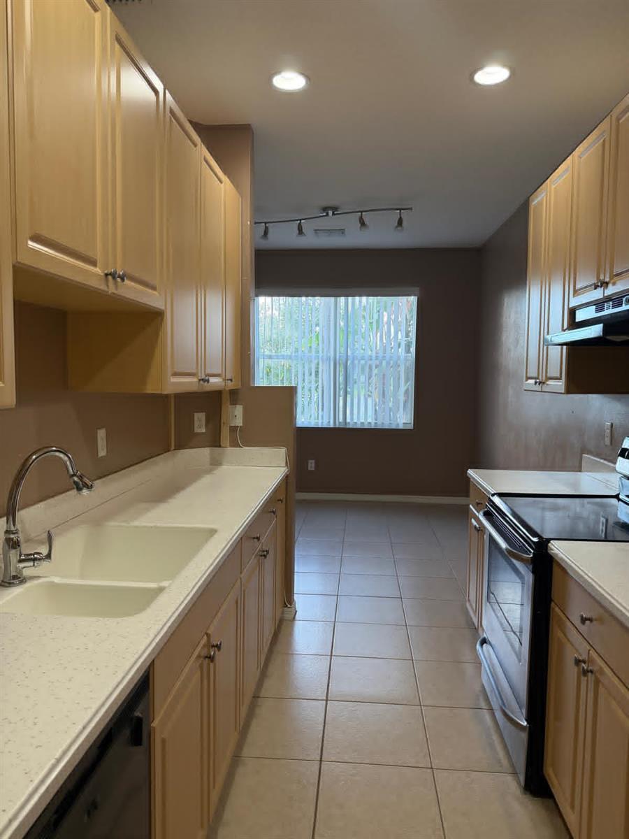 A galley kitchen features light wood cabinets, white countertops, tile flooring, and a window — 1510 Seminole Palms Drive, FL 33463, FL