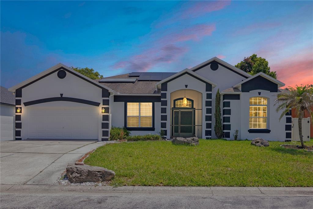 A single-story house with a white exterior, dark trim, a two-car garage, and solar panels — 216 BOXWOOD DRIVE, DAVENPORT, FL