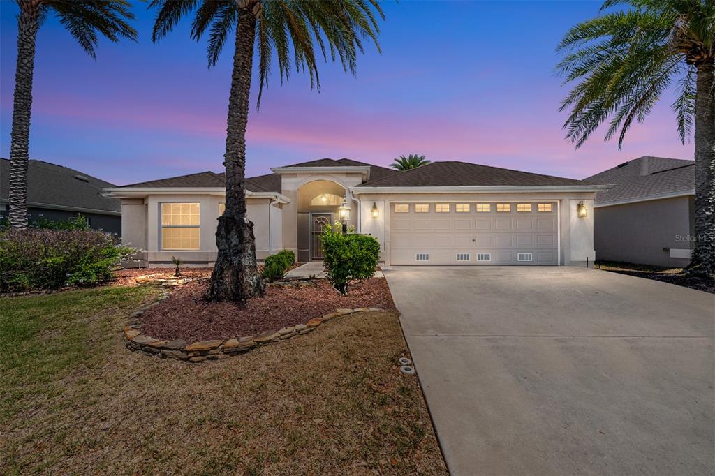 A single-story house with a two-car garage, palm trees, and a concrete driveway at dusk — 2033 SALMON WAY, THE VILLAGES, FL