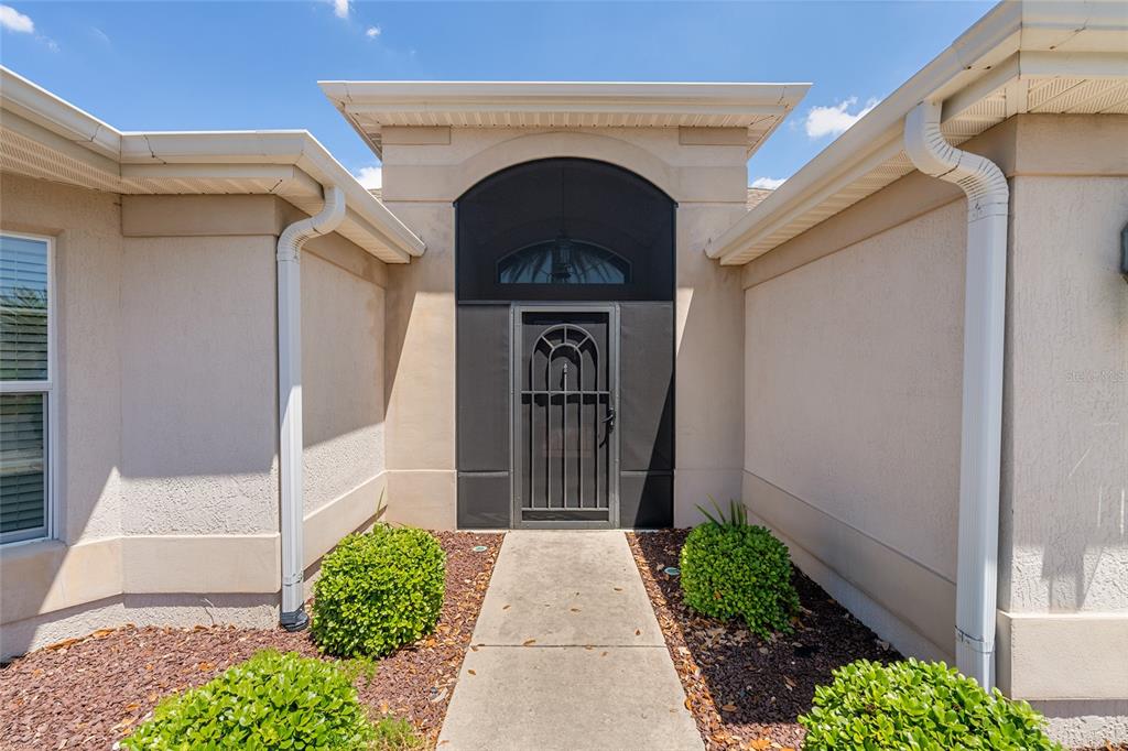 A concrete walkway leads to a front entrance with a dark screen door and archway — 2033 SALMON WAY, THE VILLAGES, FL