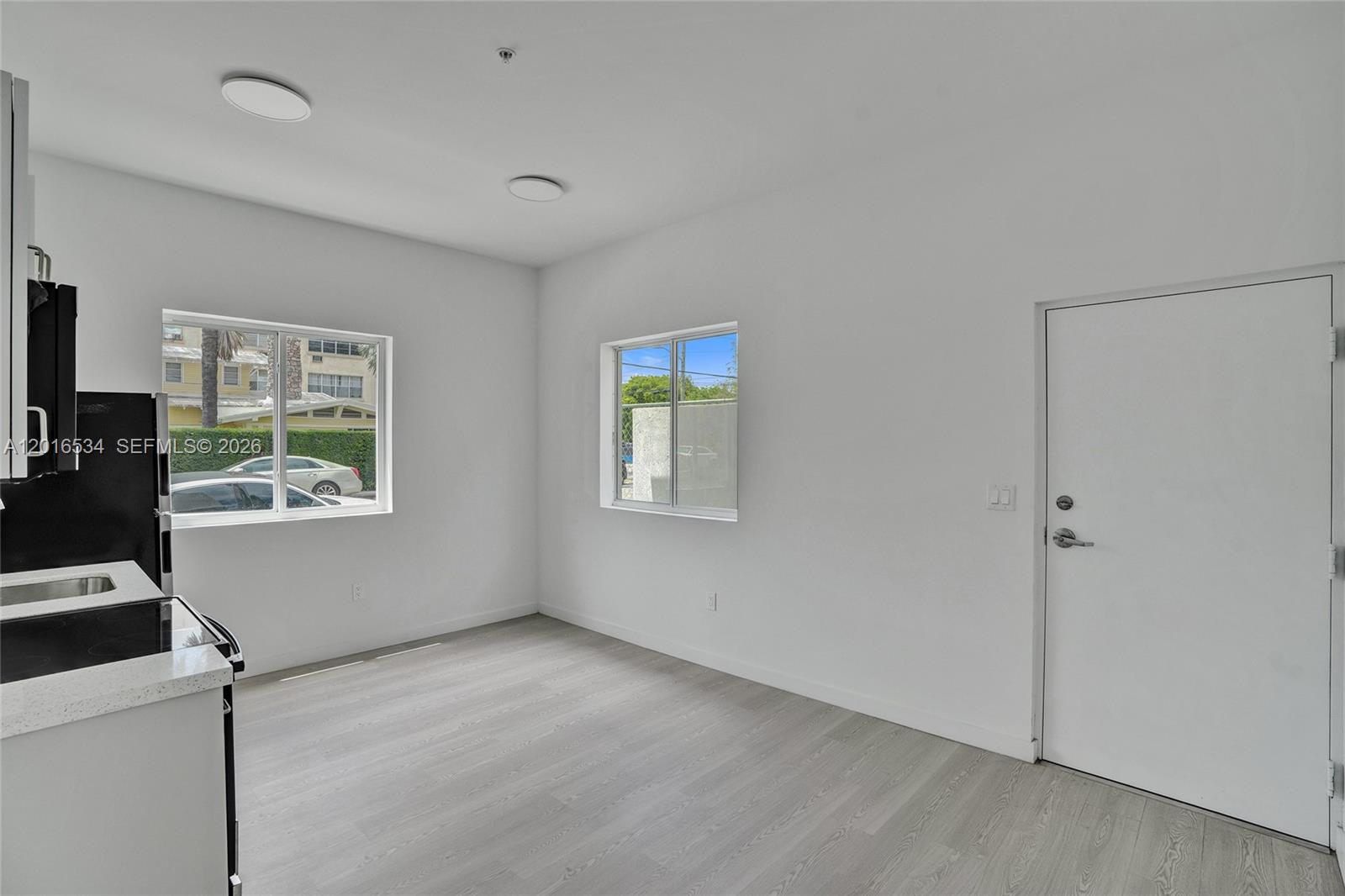 A bright, minimalist kitchen area features white walls, light wood-look flooring, and two windows — 1567 NW 1st St # 1, Miami FL 33125, MIAMI, FL