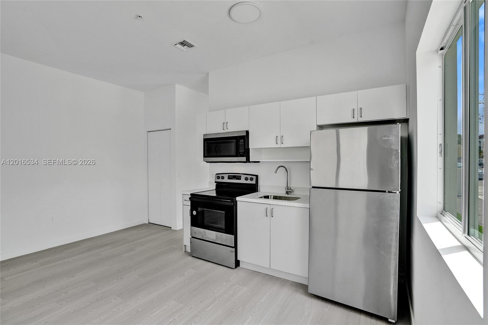 A modern kitchen features white cabinets, stainless steel appliances, and light wood-look flooring — 1567 NW 1st St # 1, Miami FL 33125, MIAMI, FL