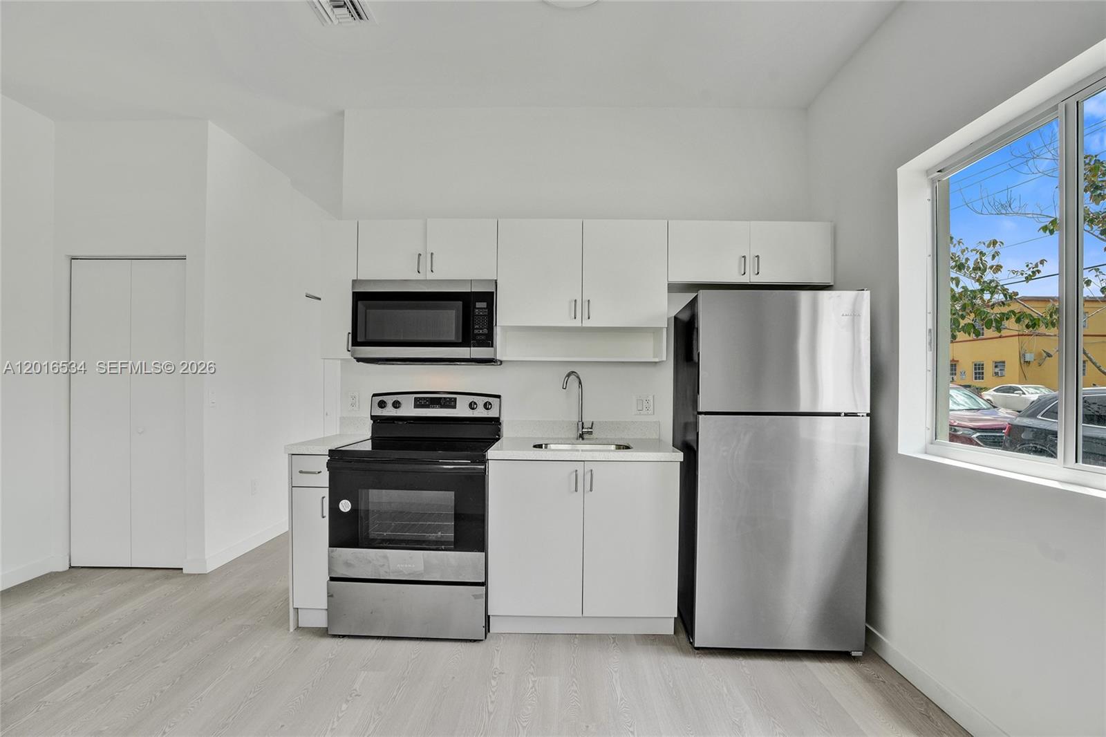 A small kitchen features white cabinets, stainless steel appliances, and light wood-look flooring — 1567 NW 1st St # 1, Miami FL 33125, MIAMI, FL