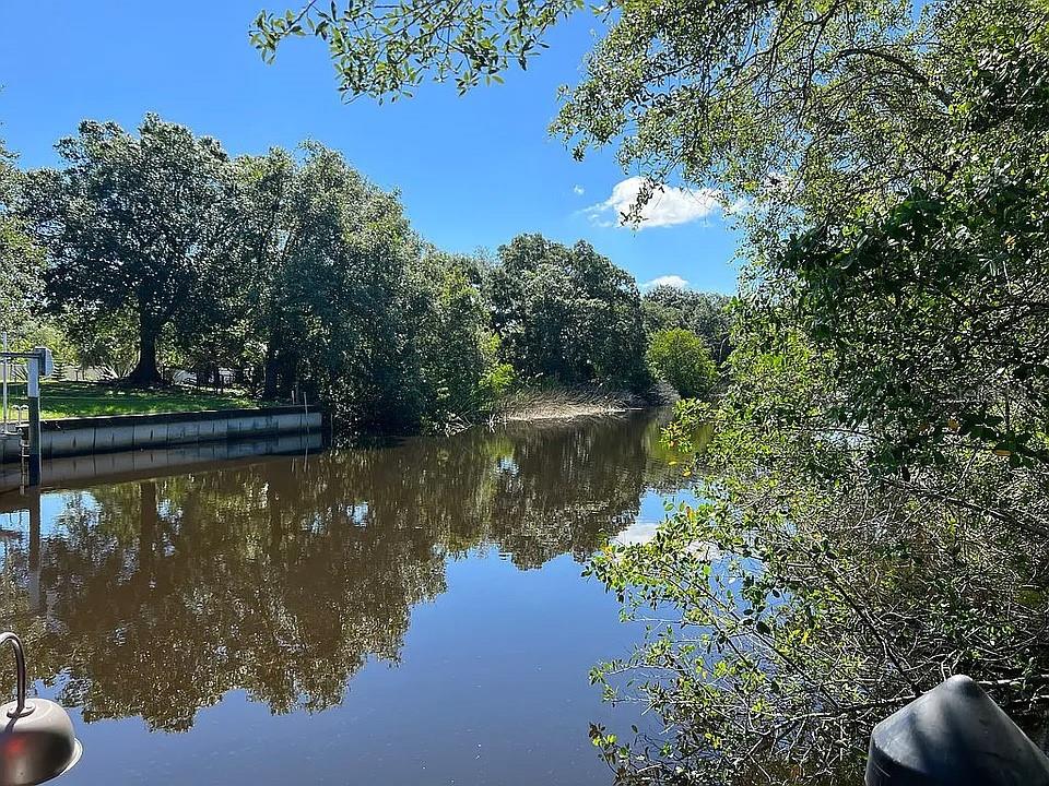 A view of a calm canal bordered by lush green trees and a concrete bulkhead — 27354 SAN CARLOS DRIVE, PUNTA GORDA, FL