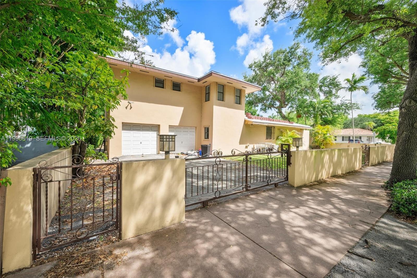 A two-story tan house with a gated driveway and a surrounding perimeter wall — 1545 Cantoria Ave, Coral Gables FL 33146, CORAL GABLES, FL