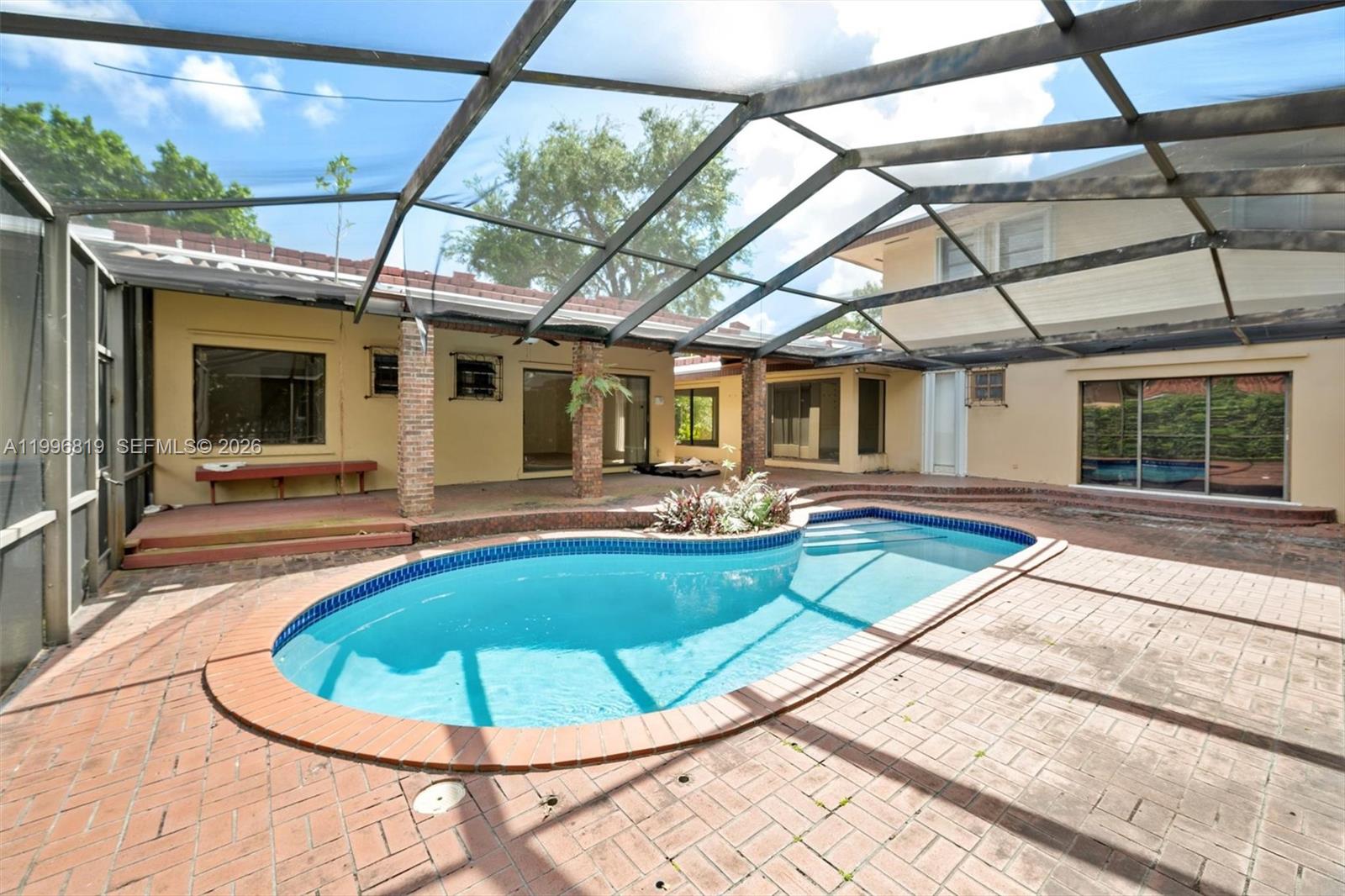 An enclosed patio features a kidney-shaped swimming pool surrounded by red brick pavers — 1545 Cantoria Ave, Coral Gables FL 33146, CORAL GABLES, FL