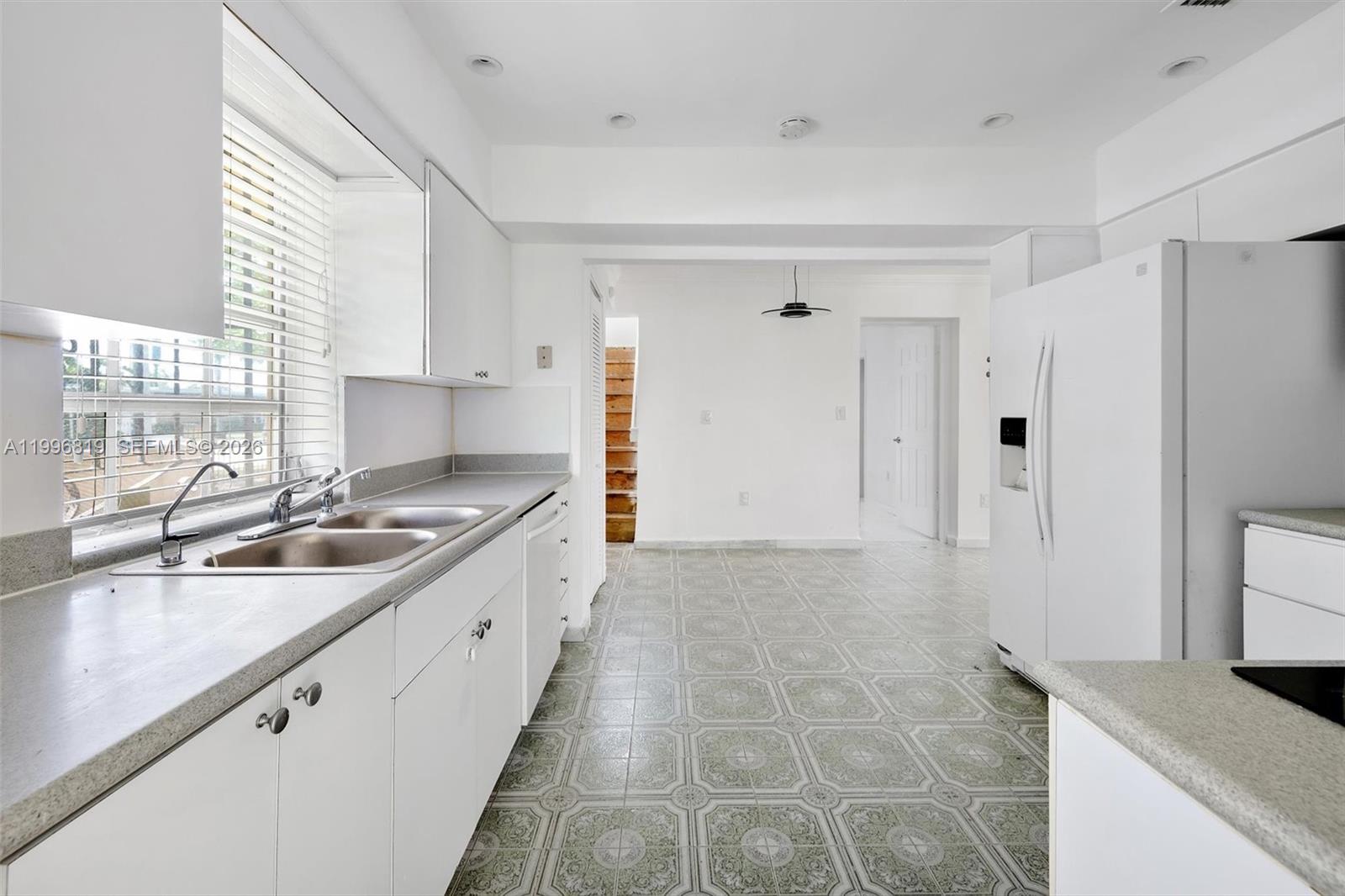 A white kitchen features a double sink, tiled flooring, and a view of wooden stairs — 1545 Cantoria Ave, Coral Gables FL 33146, CORAL GABLES, FL