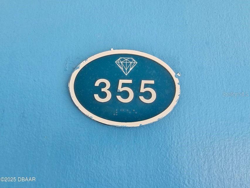 An oval blue sign with a diamond icon and the number 355 is mounted on a wall — 935 S ATLANTIC AVENUE UNIT 355, DAYTONA BEACH, FL