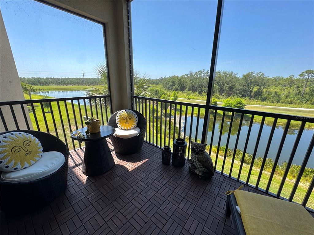 A screened-in balcony features dark wicker chairs, a small table, and views of a pond — 18028 GAWTHROP DRIVE UNIT 303, BRADENTON, FL