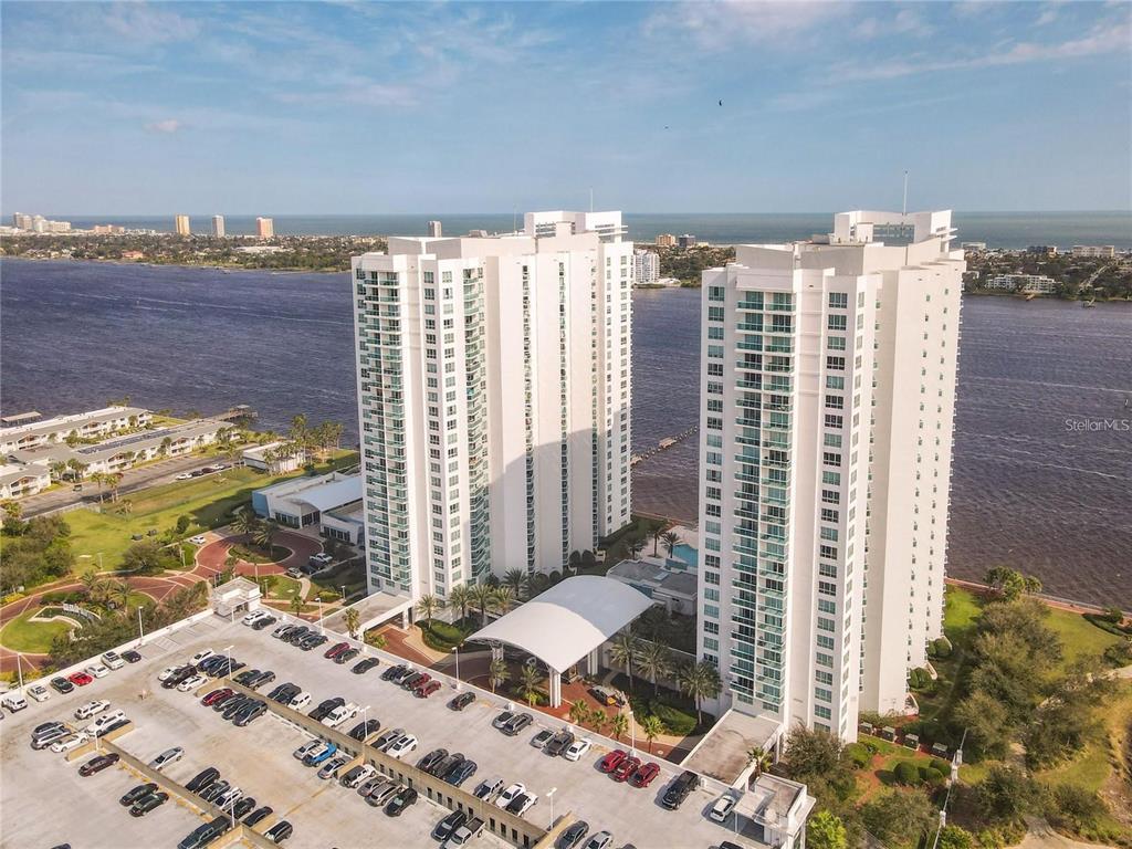 An aerial view shows two tall white residential towers situated beside a large body of water — 241 RIVERSIDE DRIVE UNIT 1809, DAYTONA BEACH, FL