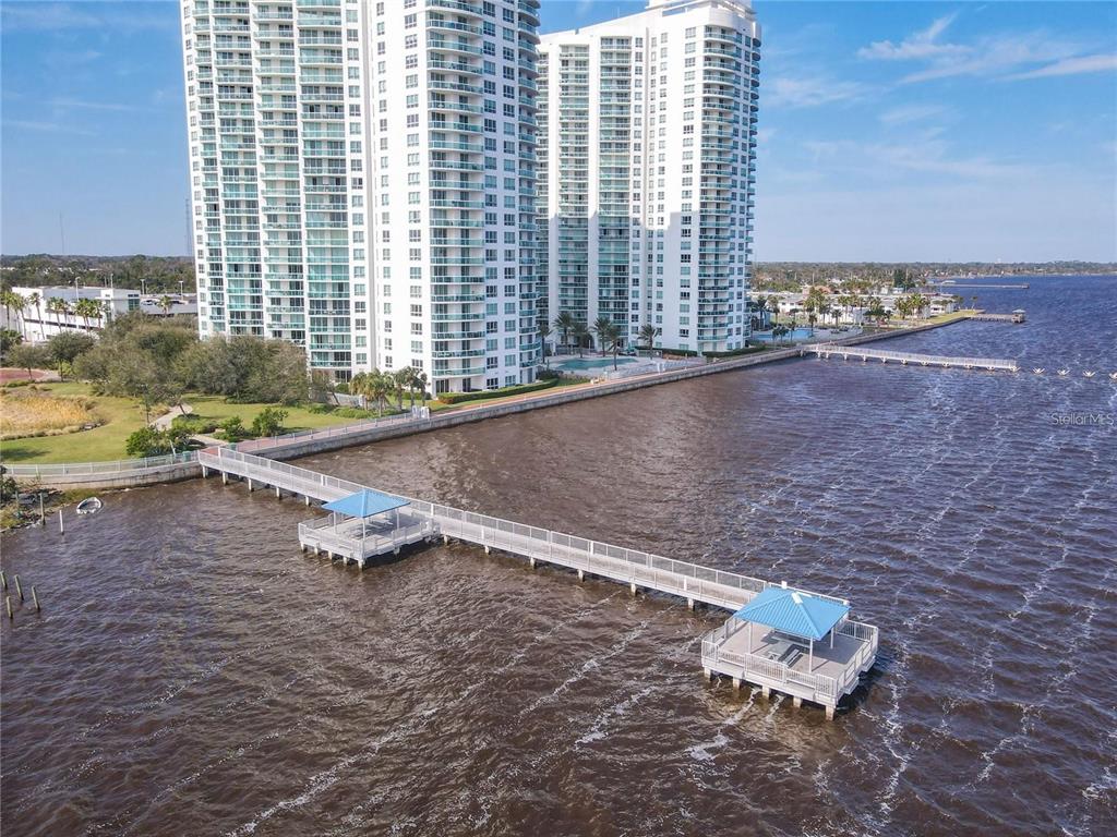 An aerial view shows a long pier extending into a bay near tall residential buildings — 241 RIVERSIDE DRIVE UNIT 1809, DAYTONA BEACH, FL
