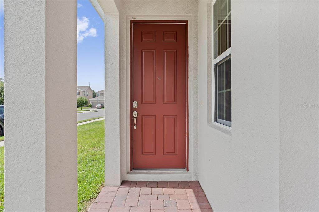 A red front door is set within a white stucco entryway with a brick walkway — 1678 SWAN SWIM DRIVE, DAVENPORT, FL
