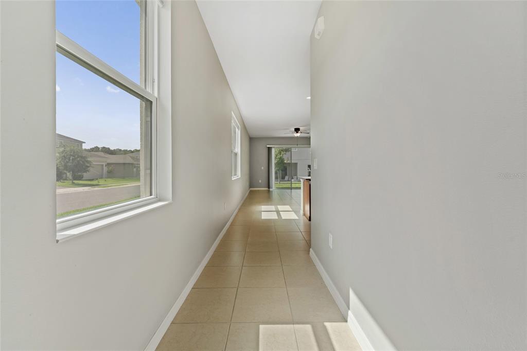 A long hallway with light-colored tile flooring leads toward a bright living area with sliding doors — 1678 SWAN SWIM DRIVE, DAVENPORT, FL