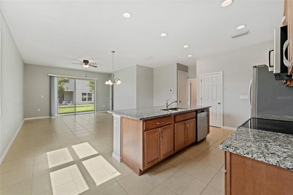 A kitchen with granite countertops and wood cabinets overlooks an open living area with tile — 1678 SWAN SWIM DRIVE, DAVENPORT, FL